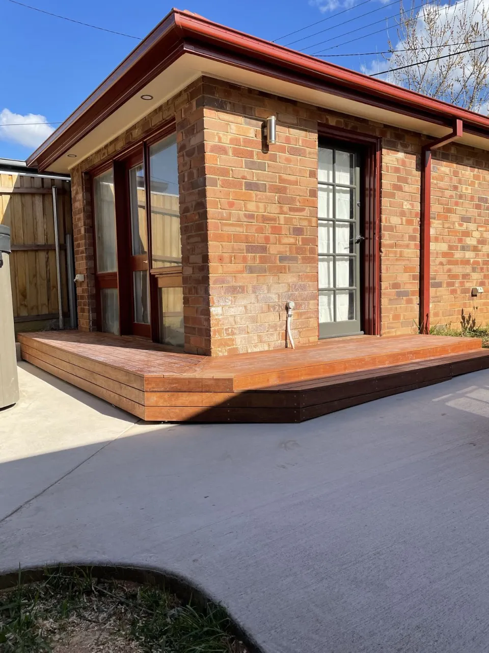 Completed cottage exterior refresh with new hardwood deck, red guttering and fascia under a bright blue sky